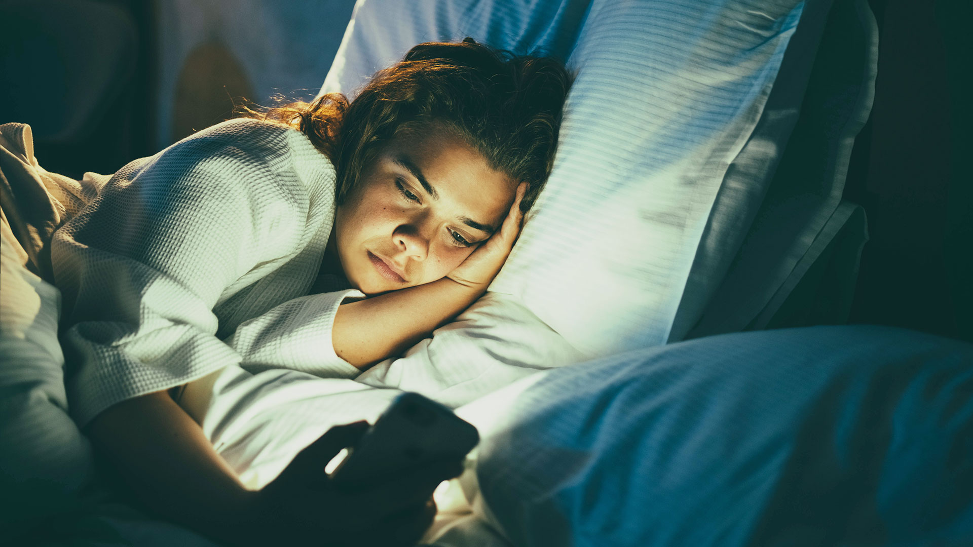 Young woman scrolling her phone in bed at night